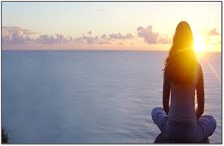 a woman meditating in front of an ocean with the sun on the horizon 
