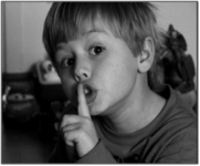A boy with his finger to his mouth, shushing, referencing mindful meditation
